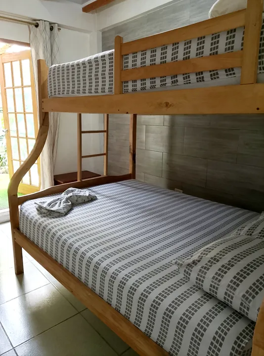 Camarote de madera con cama doble abajo y cama sencilla arriba, sábanas grises a rayas y una puerta francesa hacia el jardín