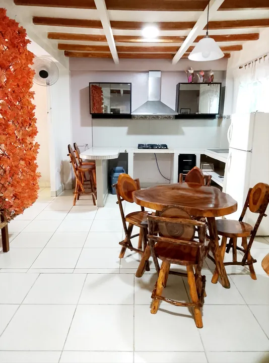Cocina abierta y comedor del apartamento con mesa redonda de madera, sillas talladas, taburetes, campana extractora, refrigeradora y un biombo de hojas anaranjadas