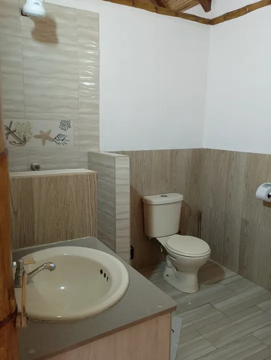 Baño de la cabaña familiar con lavabo, inodoro y ducha con azulejos decorados con conchas marinas