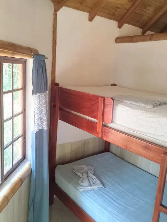 Camarote de madera con sábanas celestes junto a una ventana con cortina azul, bajo un techo de madera