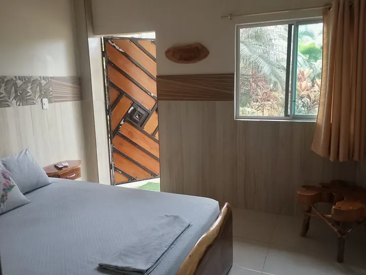 Dormitorio de la suite familiar con cama de sábanas grises, ventana con cortina y puerta de madera en espiga
