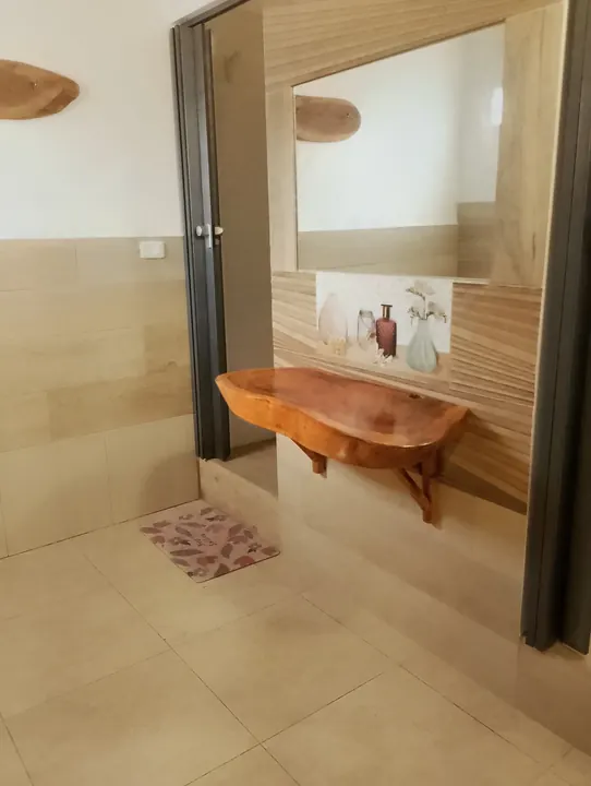 Baño con lavabo sobre una tabla de madera natural, espejo y piso de cerámica